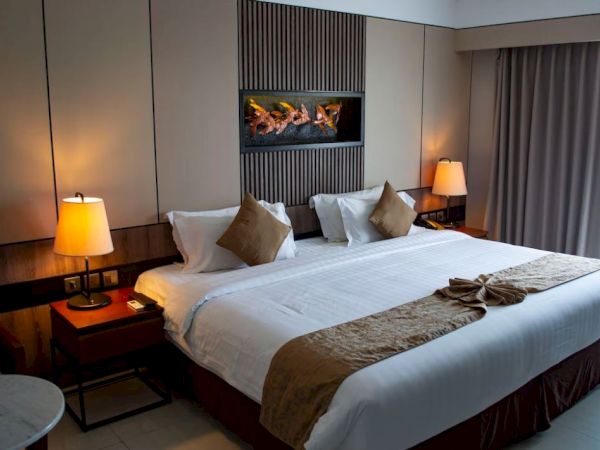 A cozy hotel room with a large bed, bedside lamps, pillows, and decor. There's a window with curtains on the right side.