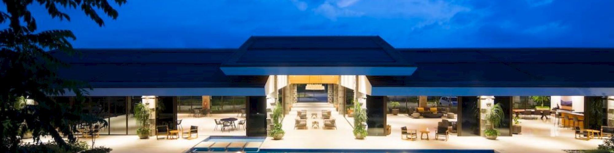 A modern building with a large illuminated pool and outdoor seating against a blue evening sky.