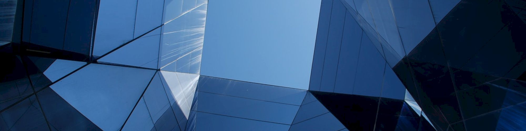 The image shows a geometric architecture view from below, with reflective glass panels and a clear blue sky at the center.