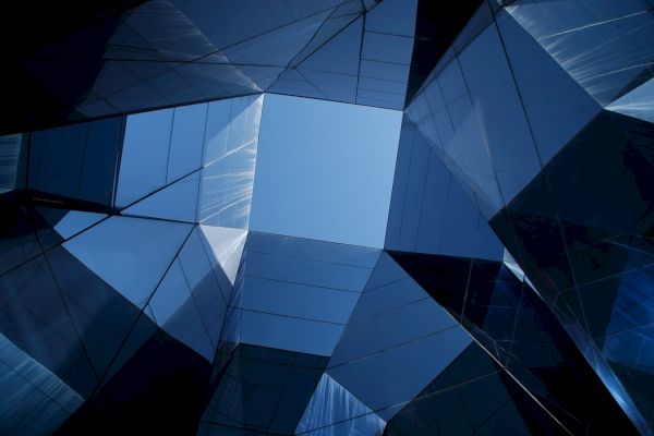 A view of the sky through modern, reflective glass buildings creating geometric patterns against the blue sky.