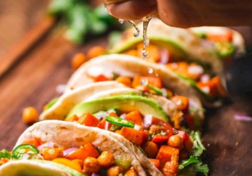 A hand squeezes lime over tacos filled with chickpeas, avocado, and veggies on a wooden board, garnished with cilantro and lime slices.
