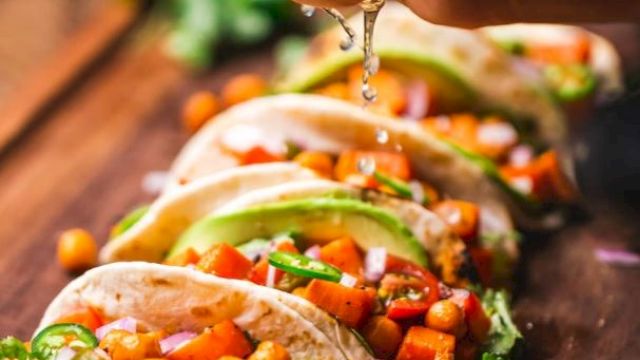 A hand squeezes lime over tacos filled with chickpeas, avocado, and veggies on a wooden board, garnished with cilantro and lime slices.