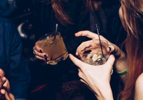 A group of people enjoying drinks and socializing in a lively setting, one person is laughing while others hold cocktails with straws.