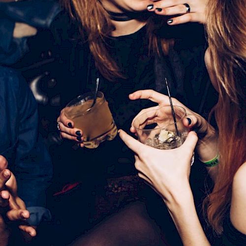A group of people enjoying drinks and socializing in a lively setting, one person is laughing while others hold cocktails with straws.