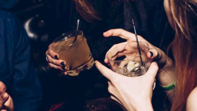 A group of people enjoying drinks and socializing in a lively setting, one person is laughing while others hold cocktails with straws.