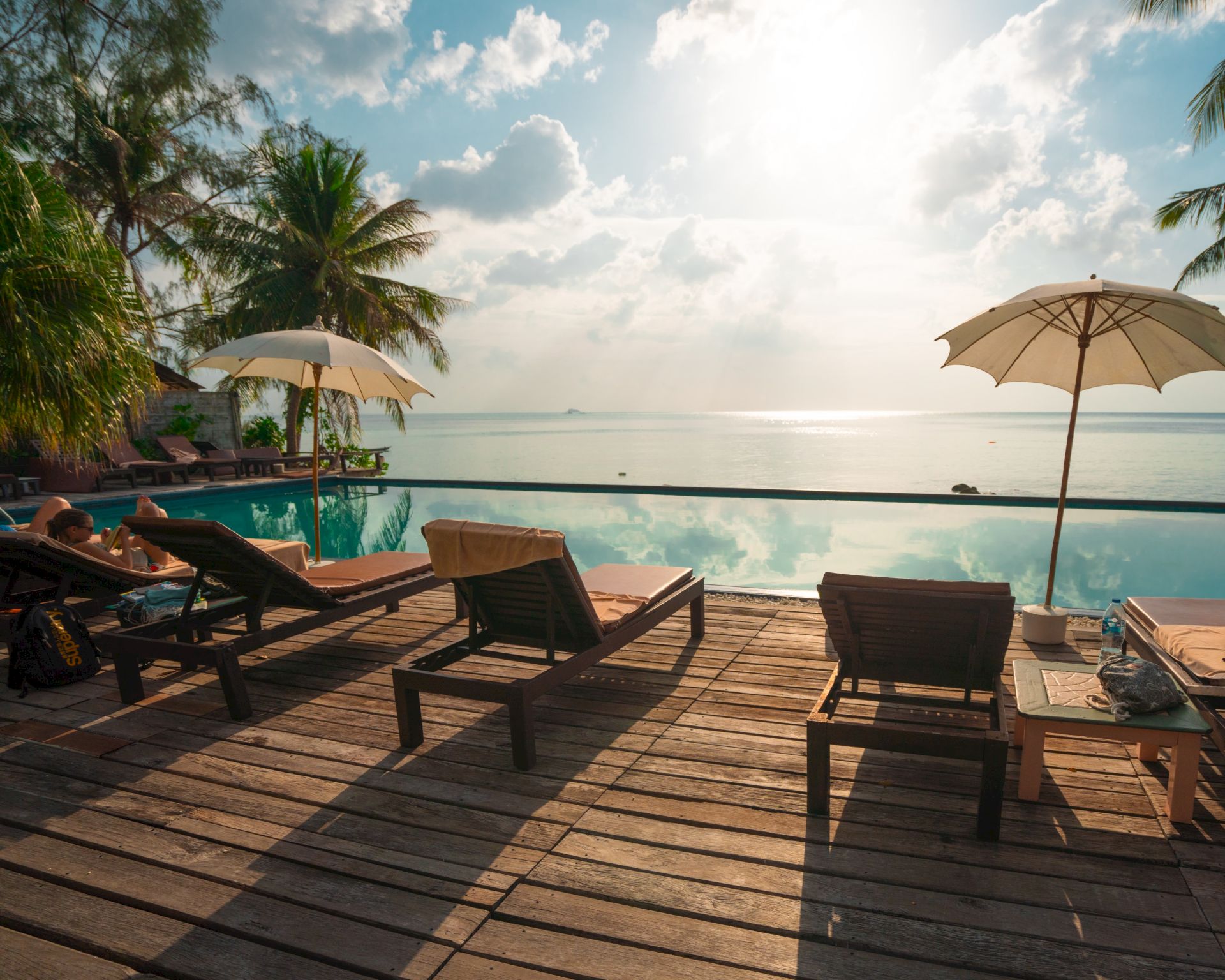 The image shows a serene beach scene with lounge chairs, umbrellas, and a stunning view of the ocean under a partially cloudy sky.