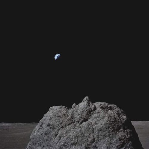 A rocky lunar surface with Earth visible in the distance against a black sky.