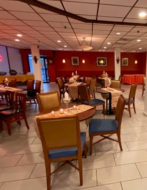 Empty restaurant dining room with tables, chairs, tiled floor, and decorated windows under warm lights.