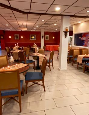 A cozy restaurant with multiple tables, chairs, warm lighting, red and blue accents, and large windows showcasing a night scene; inviting and quiet.