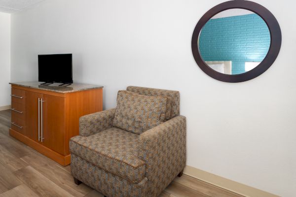 A room with a patterned armchair, wooden cabinet, flat-screen TV, and a circular mirror reflecting a blue wall.
