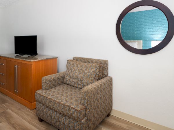 A room with a patterned armchair, wooden cabinet, flat-screen TV, and a circular mirror reflecting a blue wall.