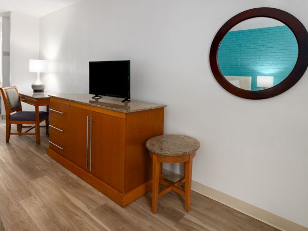 A hotel room vanity area with a flat-screen TV on a wood cabinet, a round mirror on the wall, and chairs.