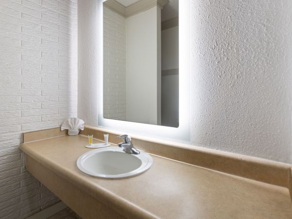 A bright bathroom vanity with a built-in sink, chrome faucet, and a large illuminated mirror above neatly arranged toiletries.