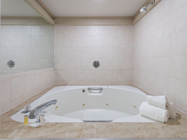A tiled bathroom with a white bathtub featuring built-in fixtures, wall jets, and a small safety grab bar, lit by a ceiling light.