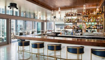 A modern bar with a well-stocked shelf, elegant seating, and large windows overlooking a cityscape completes this stylish scene.