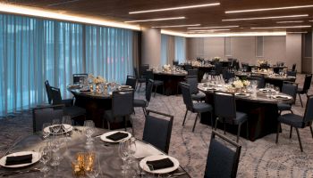 The image shows a banquet hall with round tables set for an event, featuring dim lighting and elegant table settings.