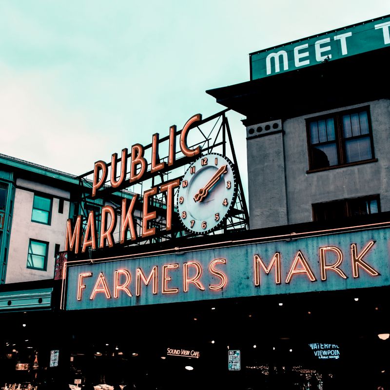 The image shows a city scene with signs for "Public Market" and "Farmers Market," featuring a clock and buildings in the background.