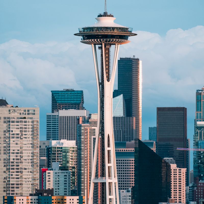 The image shows a city skyline with a prominent tower featuring a saucer-shaped top, surrounded by modern skyscrapers under a cloudy sky.