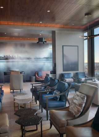 A modern lounge with plush seating, cityscape mural, large windows, and views of a Ferris wheel and water outside.