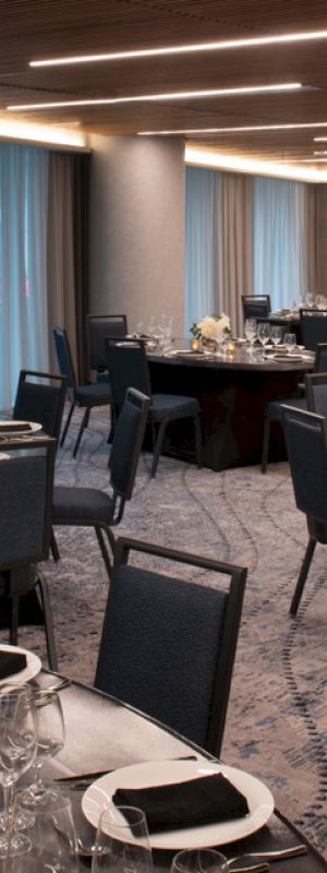The image shows an elegant banquet room set with round tables, chairs, dinnerware, and floral centerpieces, under modern lighting.
