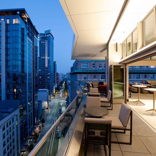 A modern rooftop terrace overlooking a cityscape at dusk, featuring outdoor seating and tables.