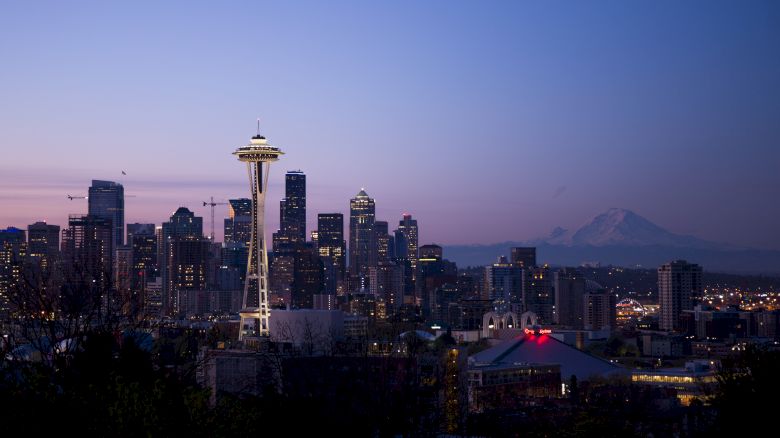 Seattle skyline at dusk featuring the Space Needle and Mount Rainier in the background, with city lights illuminating the scene.