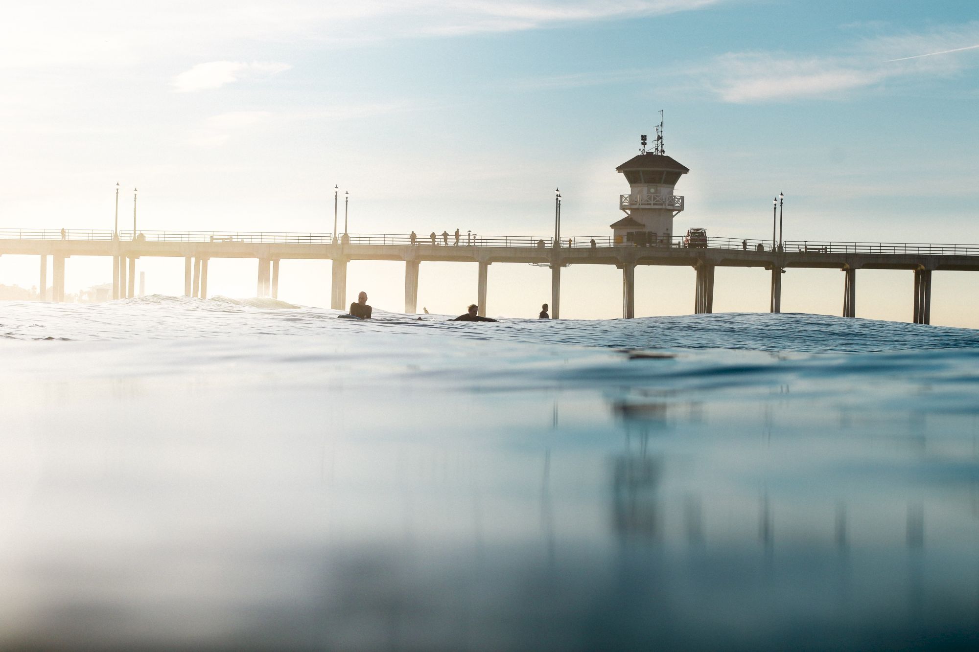 The image shows people on a pier above the ocean, with a calm sea and a clear sky in the background.